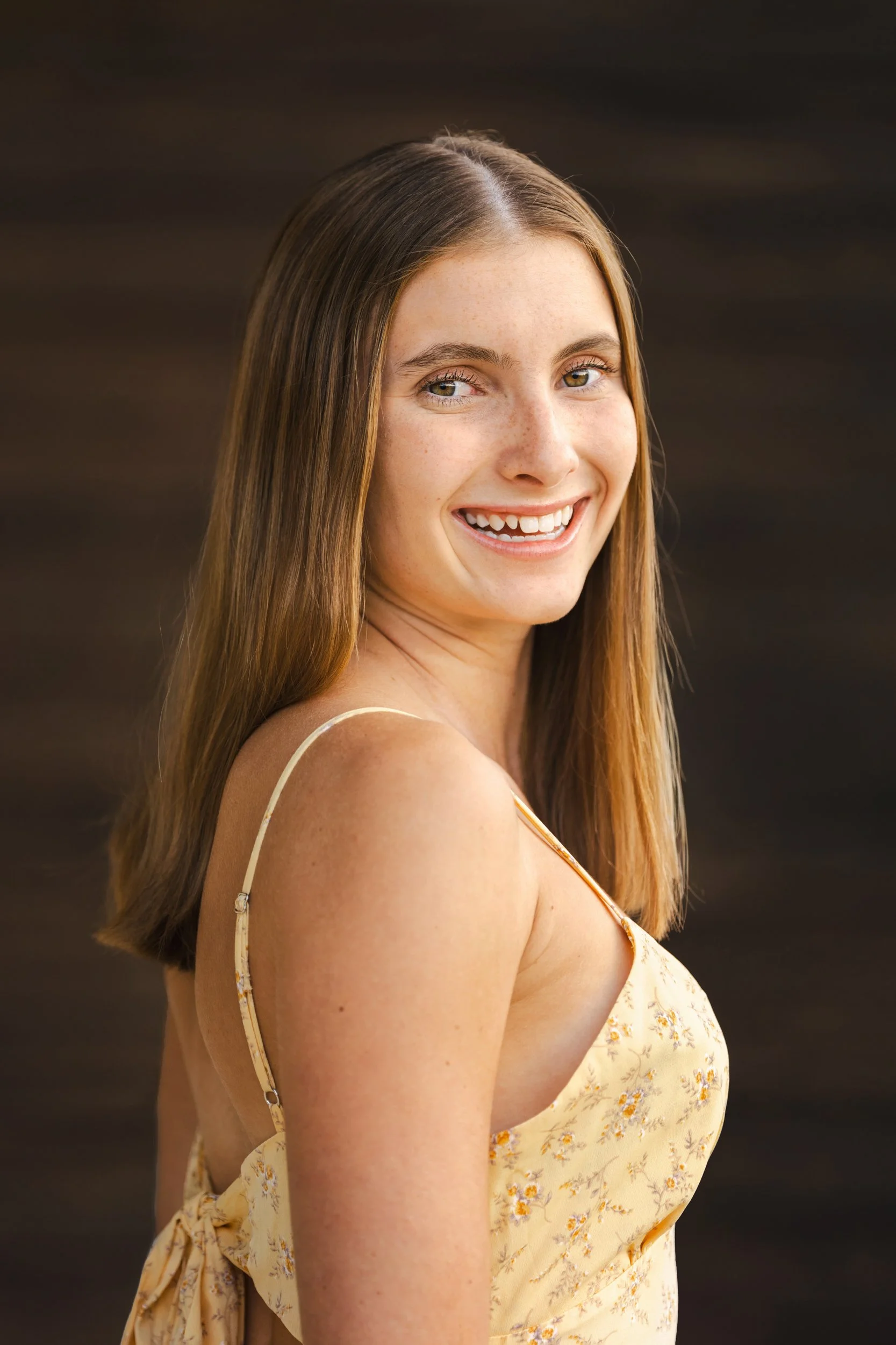 A simple dark brown wooden backdrop provides the perfect compliment to a stunning portrait of a high school senior girl.