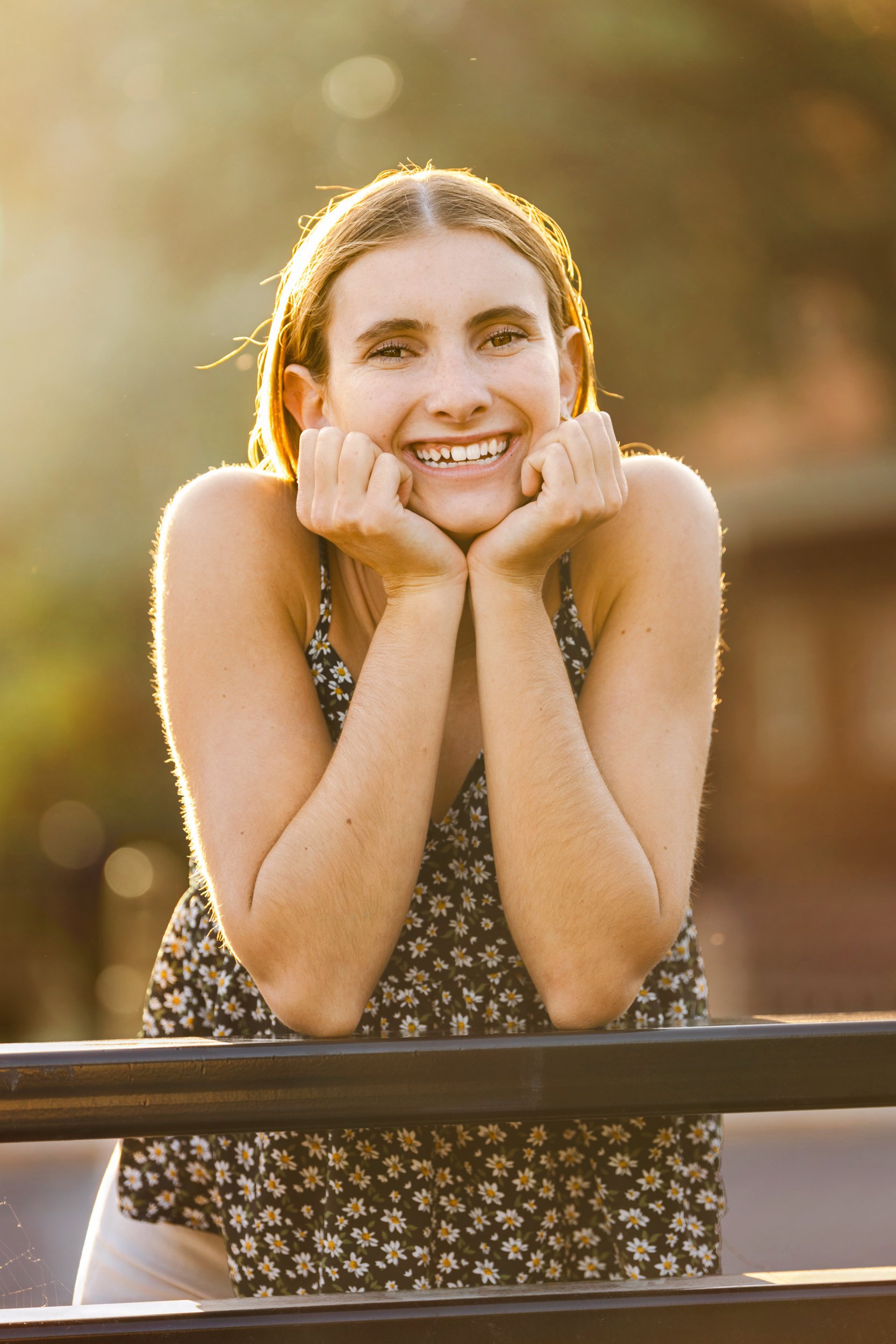 A high school senior girl smiles, leans on a railing in Buffalo, Wyoming during golden hour.
