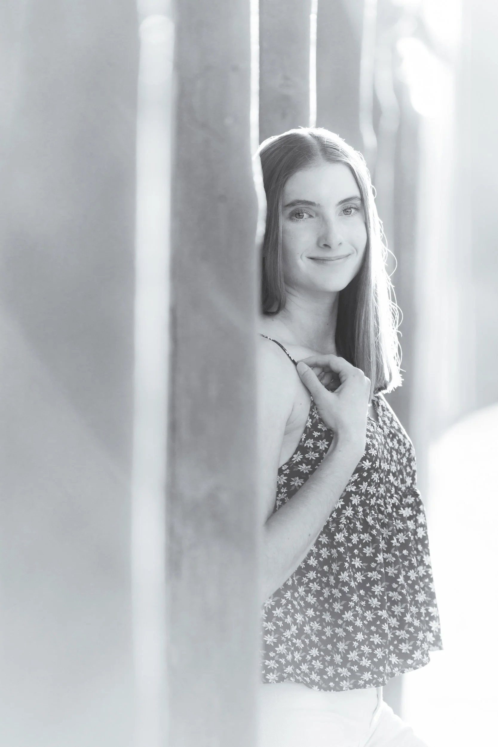 A young woman leans against a building in Buffalo, Wyoming during golden hour, smiling lightly at the camera for her high school senior photoshoot in black and white.