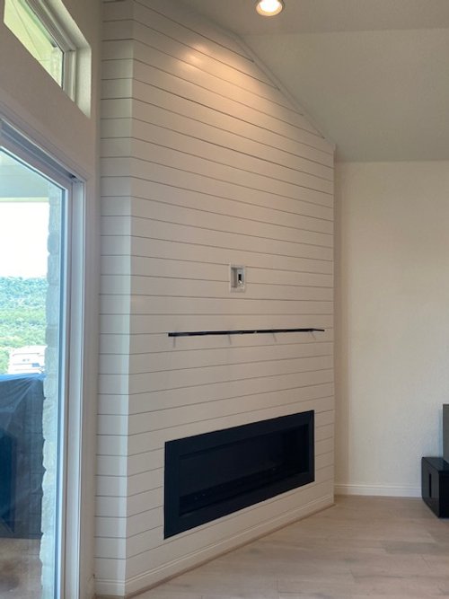 Interior wall with a shiplap finish, featuring an inset fireplace and a TV wall mount above it, next to a large window.