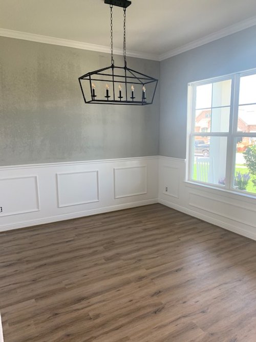 Empty room with wooden floor, gray walls, wainscoting, and a geometric chandelier.