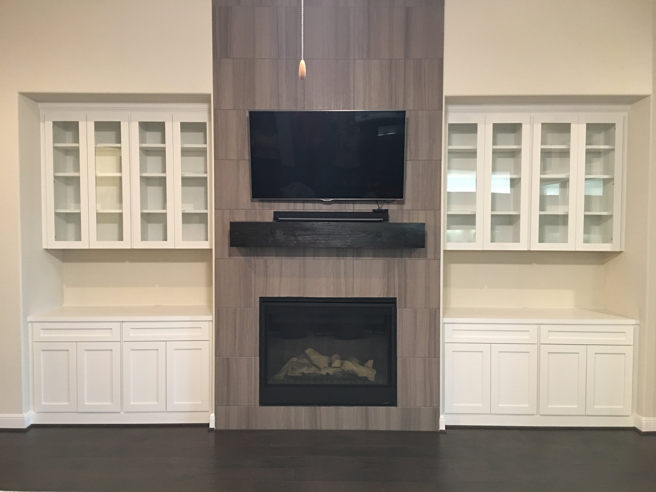 Living room interior with built-in shelves, a flat-screen TV mounted above a fireplace, white cabinets, and dark wooden flooring.