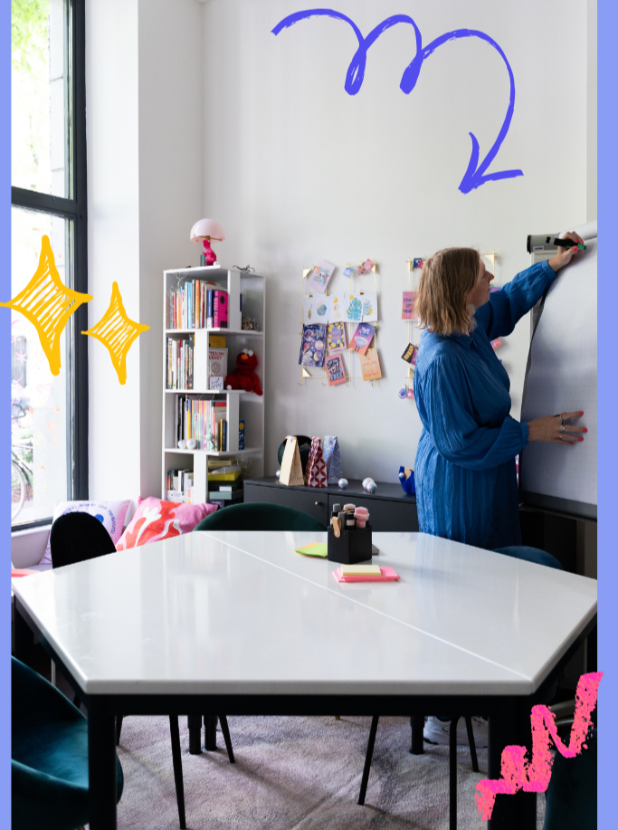 A woman writing on a whiteboard in a bright, cozy room with a bookshelf, colorful artwork, and a large window. Digital doodles include blue numbers '3' and '2', yellow stars, and pink scribbles.