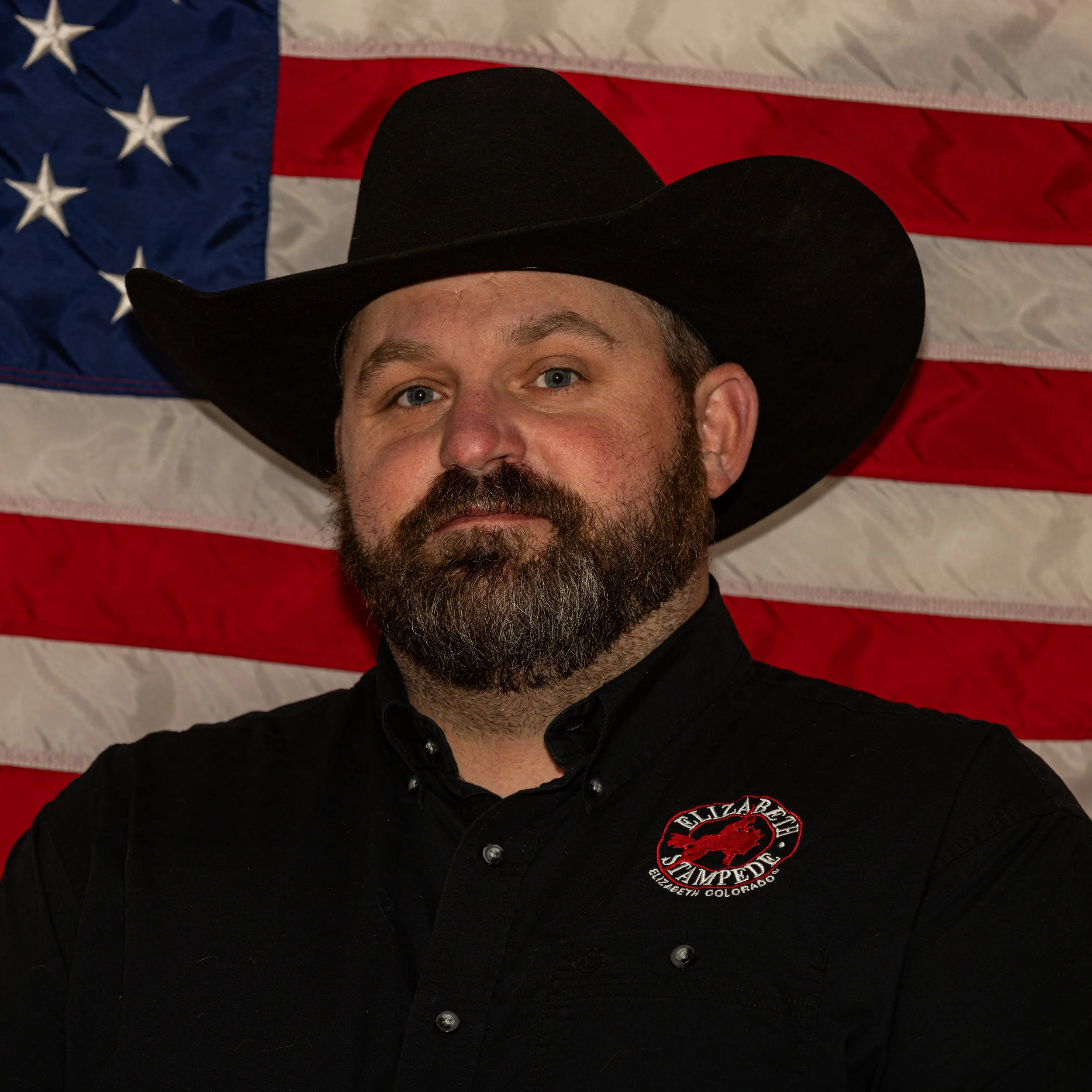 A headshot of Matt Weber wearing a black cowboy hat and red Elizabeth Stampede shirt