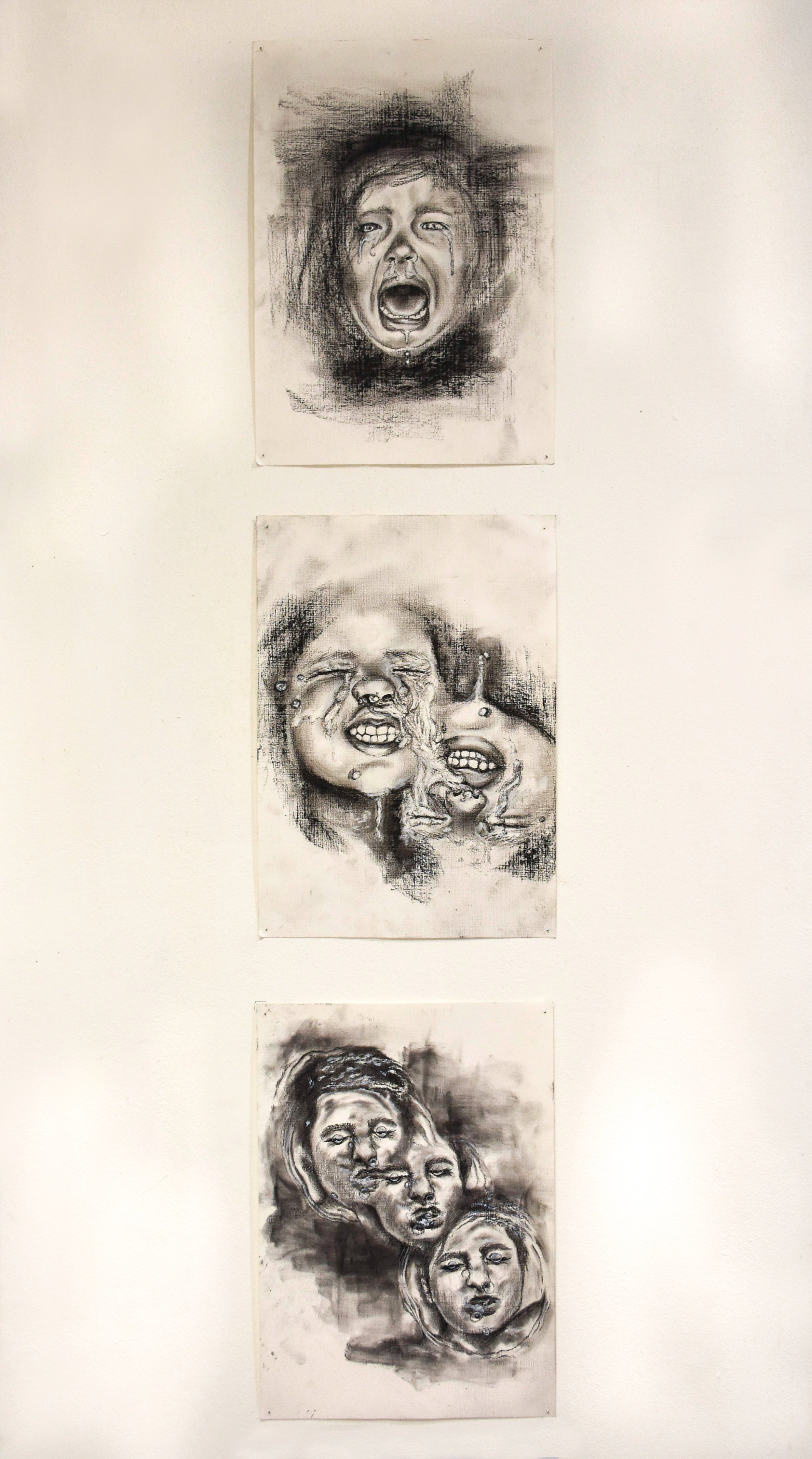 Three black-and-white emotional portraits of human faces displayed on a white wall.