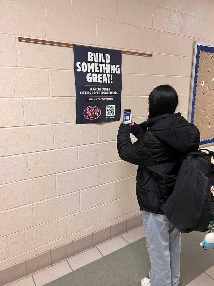 Person photographing a career advertisement poster on a wall.