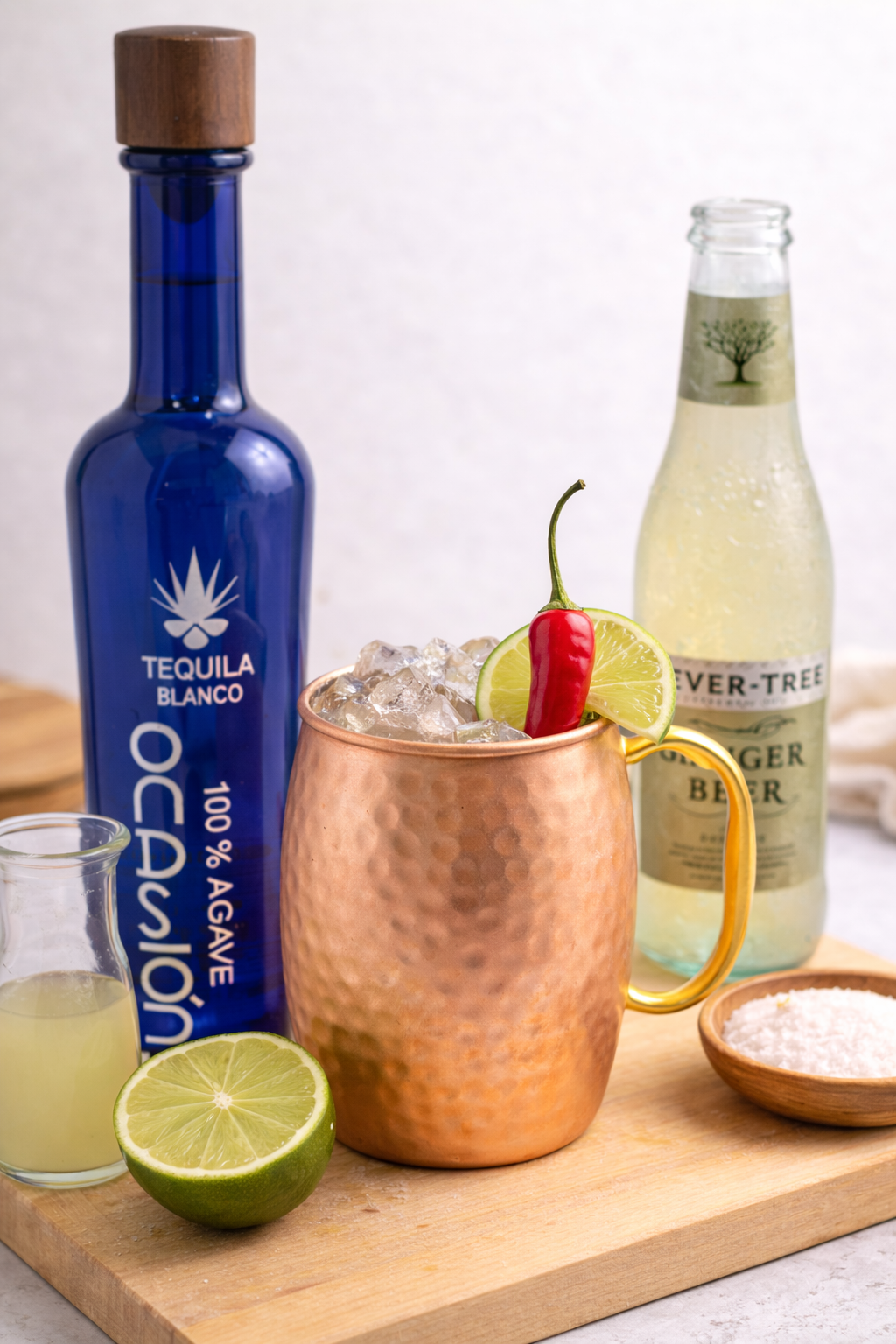 Two copper mugs filled with iced drinks garnished with lime slices and mint leaves, surrounded by lime wedges, mint sprigs, ice cubes, and a small plate with lime slices on a textured green surface.