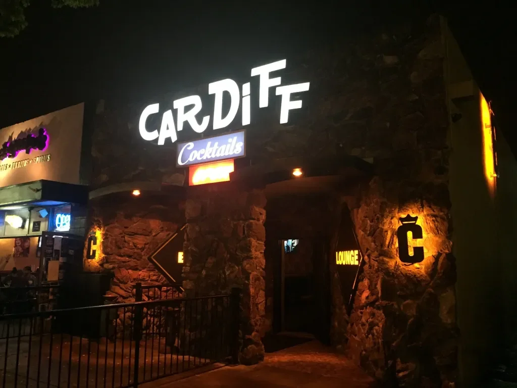 Night view of the entrance to Cardiff, a bar or lounge, with stone exterior walls, illuminated signage, and an archway entrance.