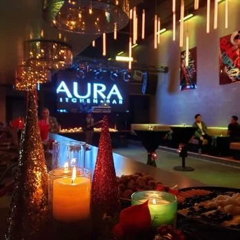Indoor entertainment venue with a pool table, illuminated decorative lighting, candles, and a large digital DJ screen displaying 'AURA' in the background.
