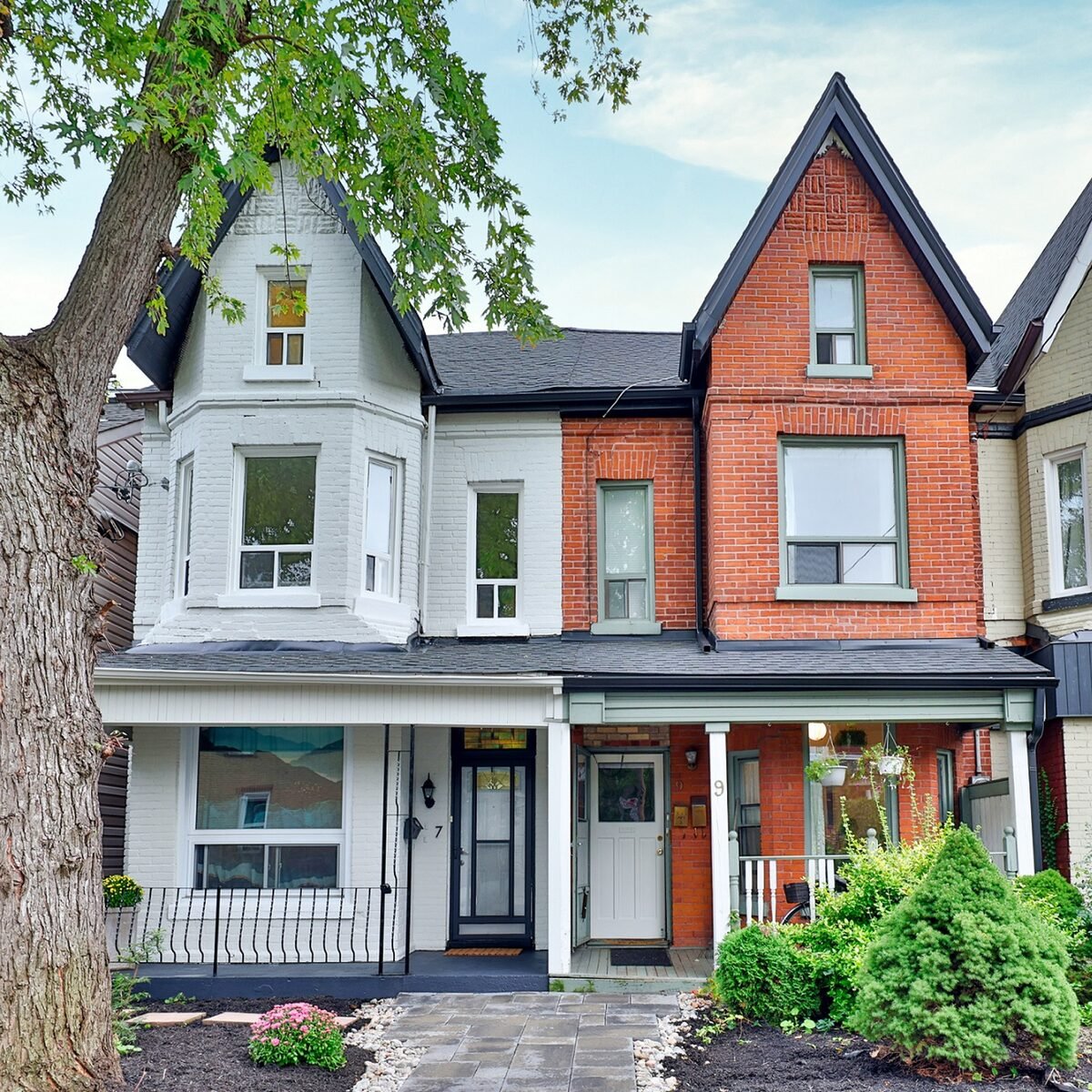 Front view of a three-story house with a combination of white and red brick exterior, featuring a porch, large windows, and a tree in the foreground, with a well-maintained garden.