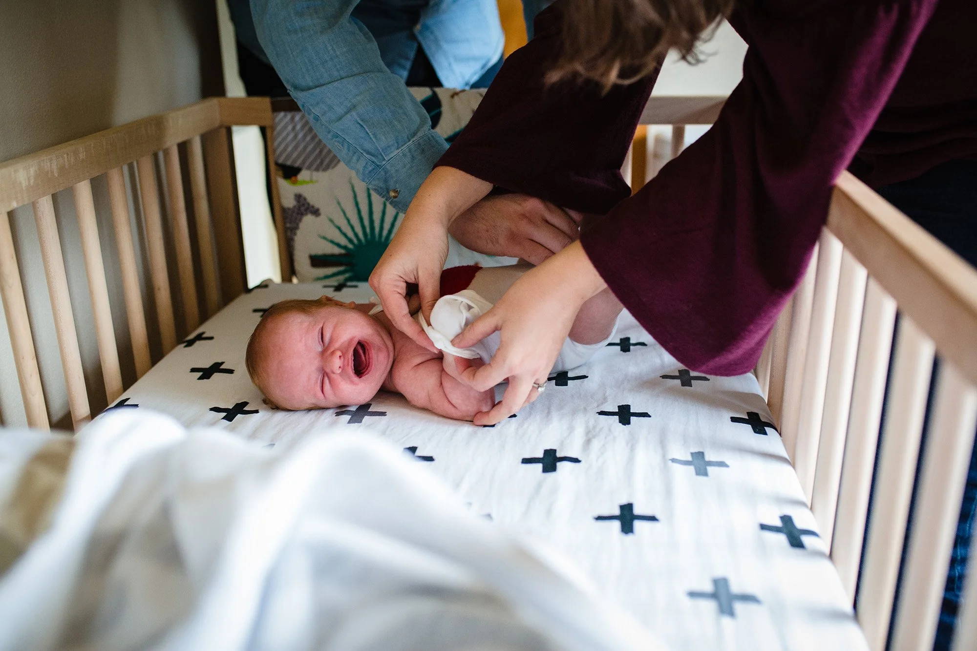 newborn baby crying in crib while mom and dad change his clothes