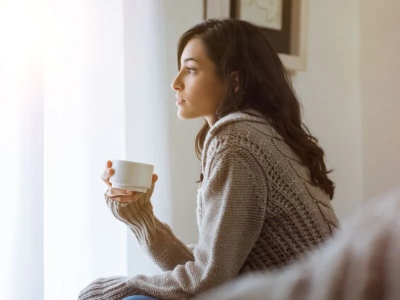 Woman sitting thoughtfully by a window, reflecting on relationships and emotions