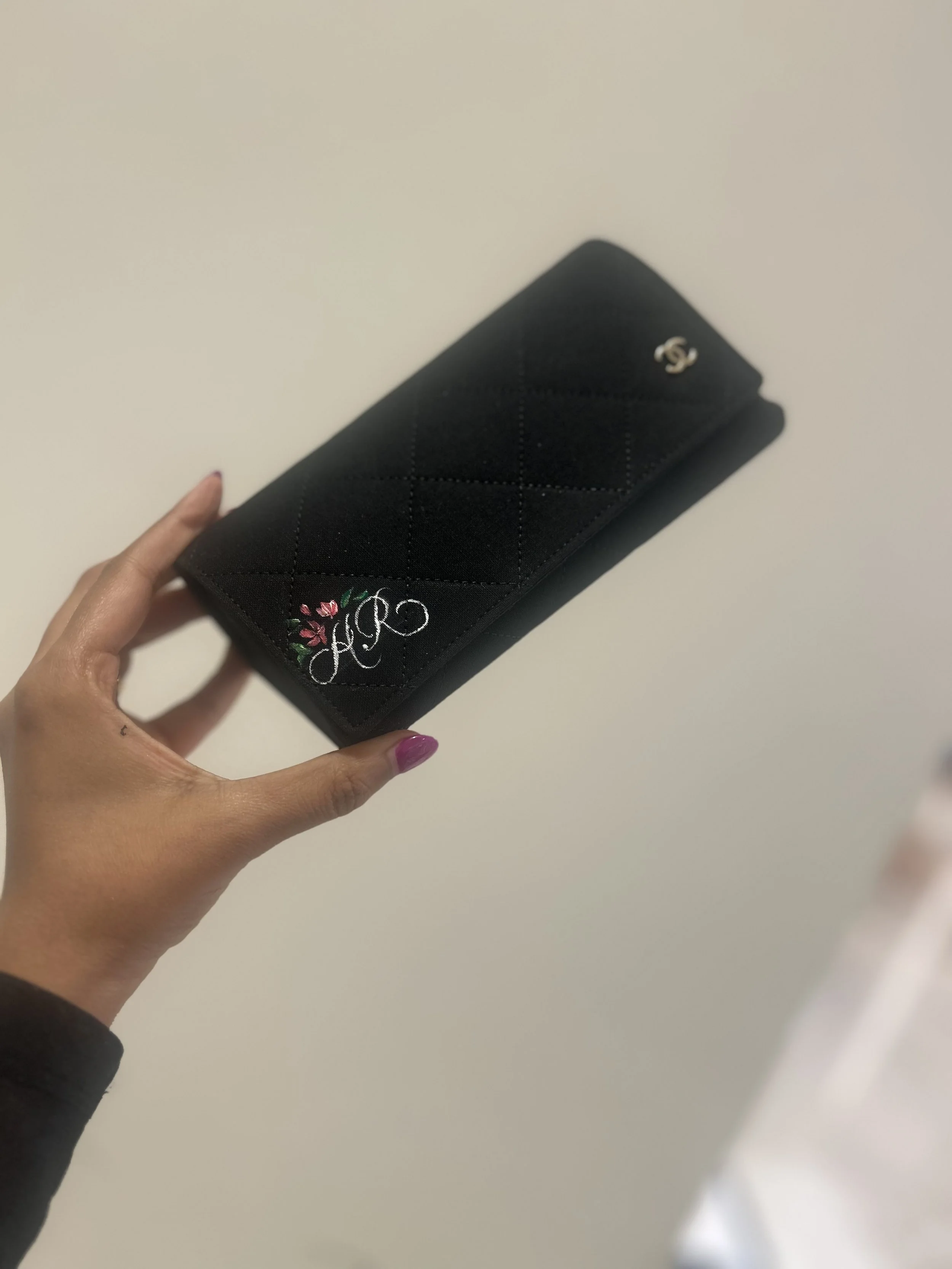 Black quilted wallet with silver Chanel logo and floral embroidered initials.