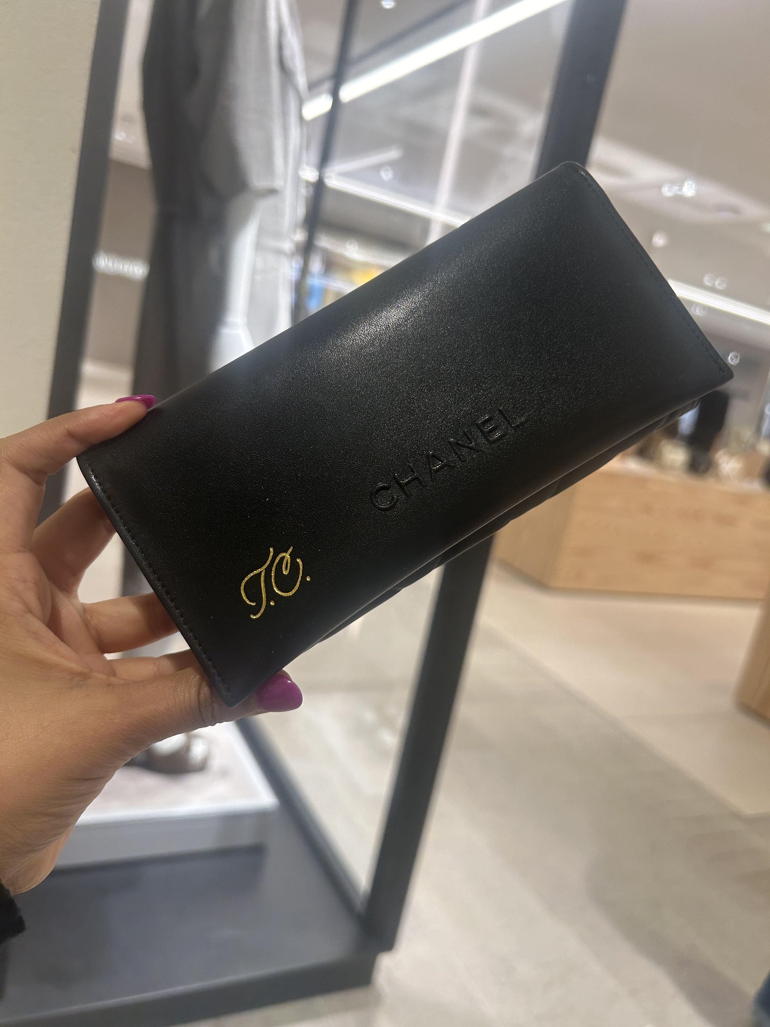A hand holding a black Chanel wallet with gold initials on it inside a store.