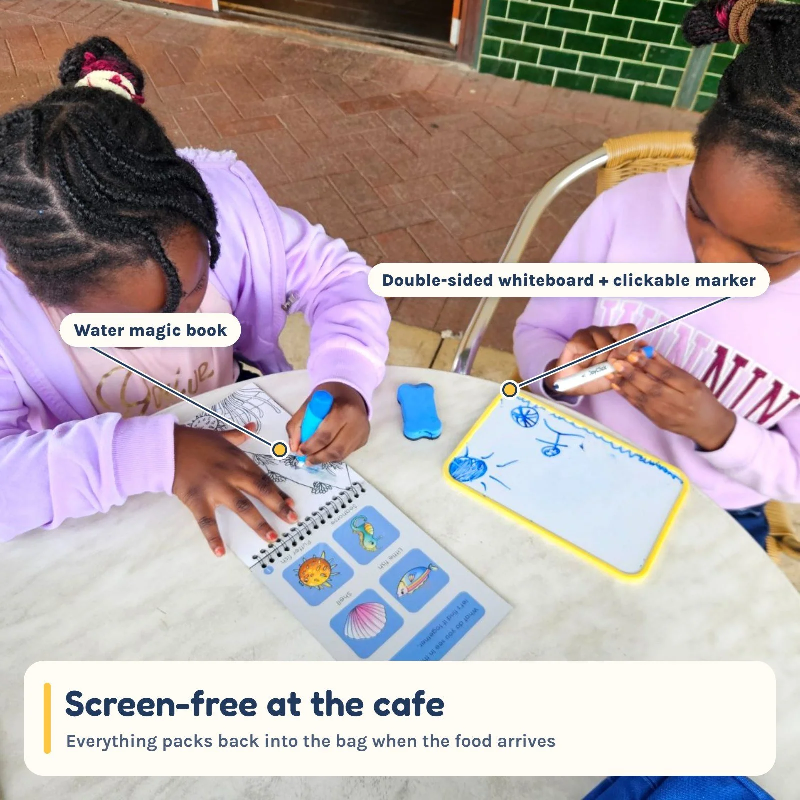 Two girls using the whiteboard and water colouring book at a cafe table