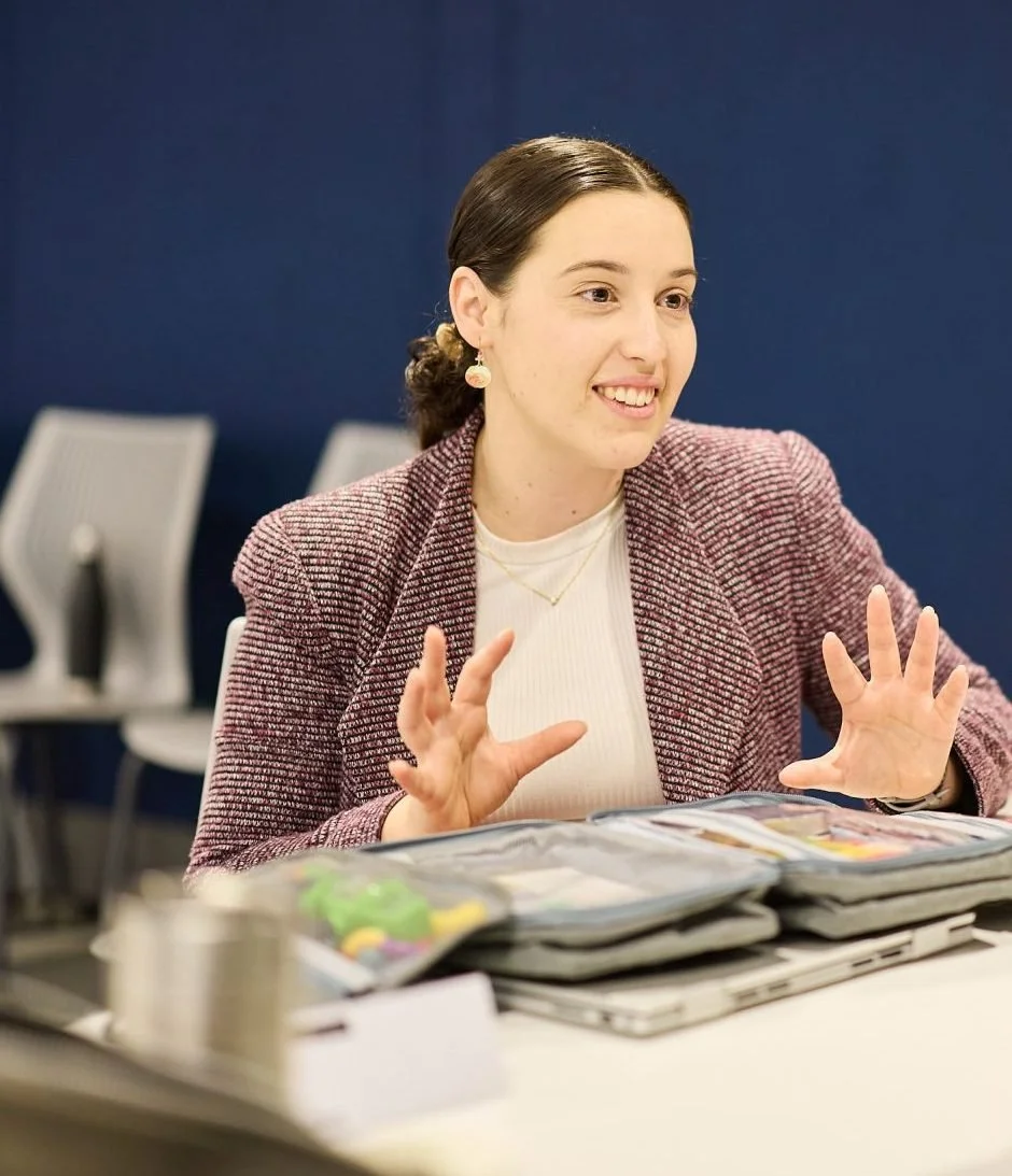 Brittany talking with another professional across a table, gesturing as she explains something
