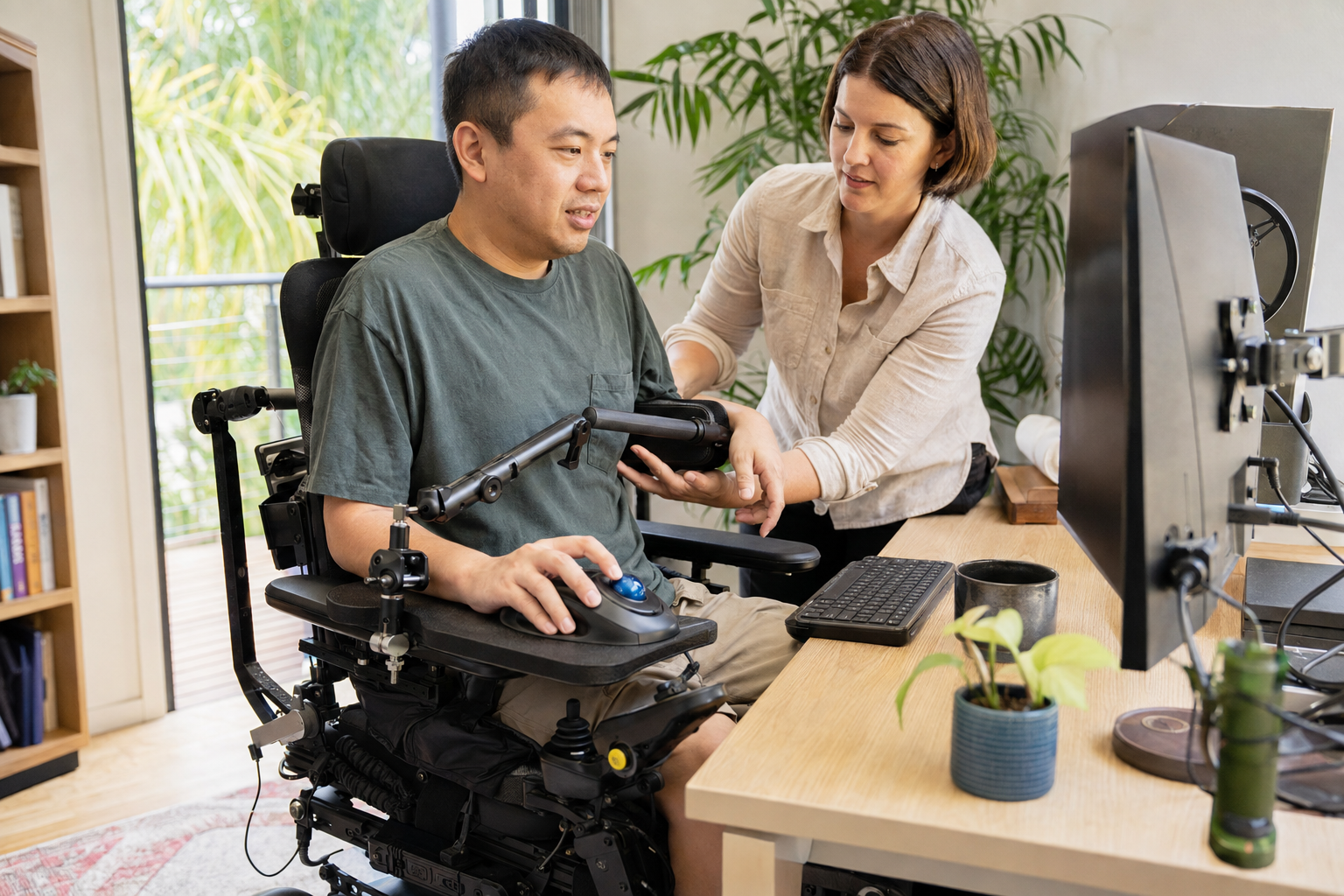 Occupational therapist adjusting workstation equipment while a participant trials an accessible trackball mouse.