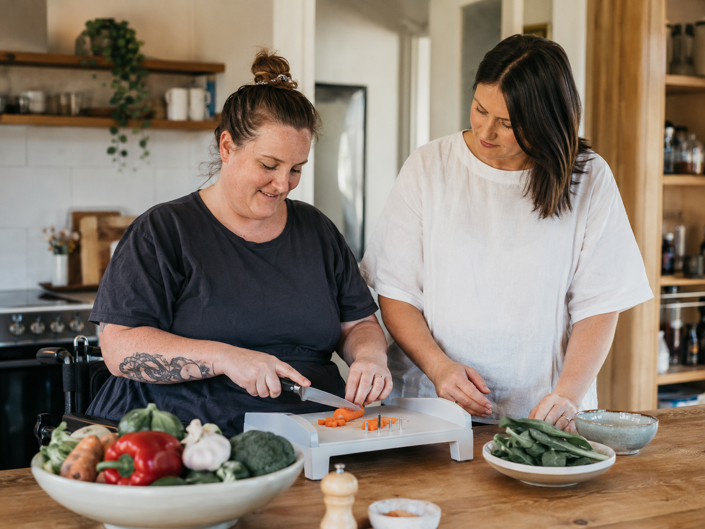 Wheelchair user preparing vegetables with guidance from an occupational therapist in a home kitchen.