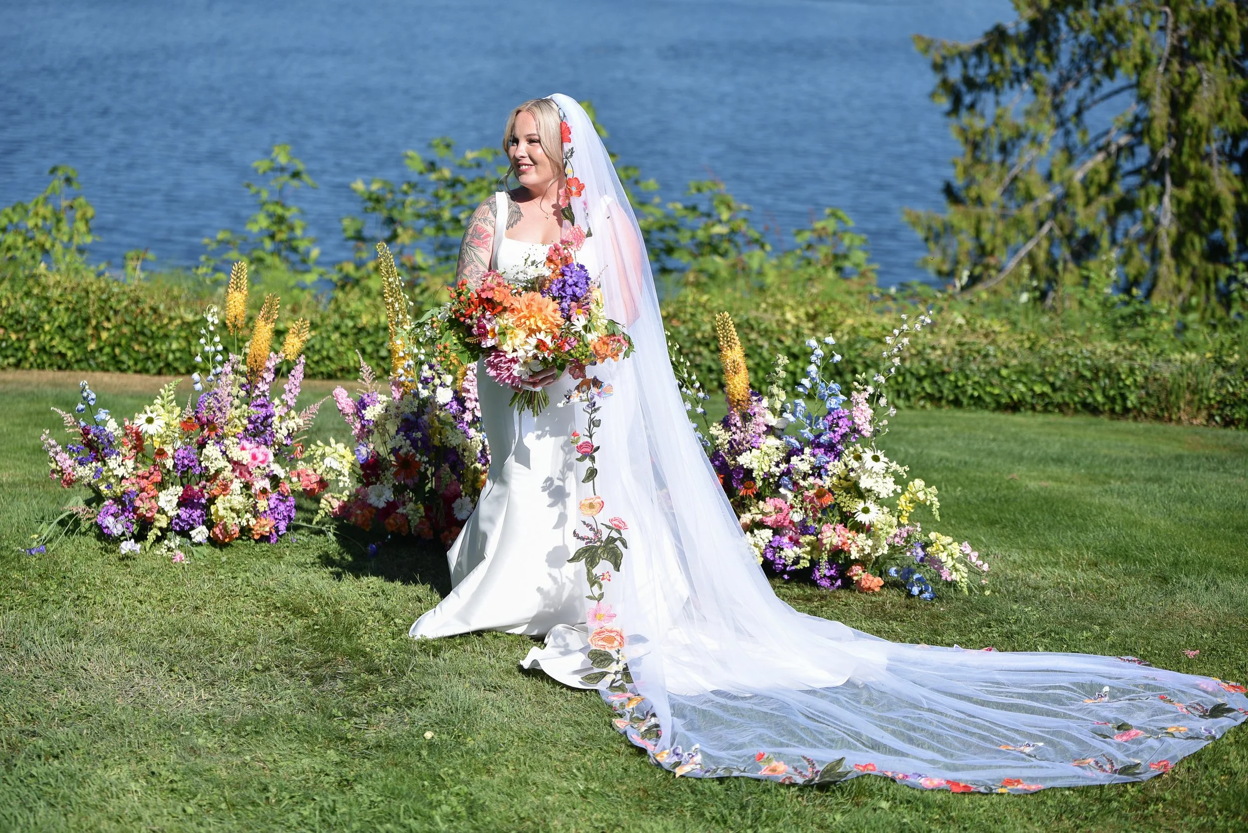 Bride with large colorful dahlia bridal bouquet in front of a garden meadow arch. Lots of dahlias, astilbe, snapdragons, crocosmia, and phlox.