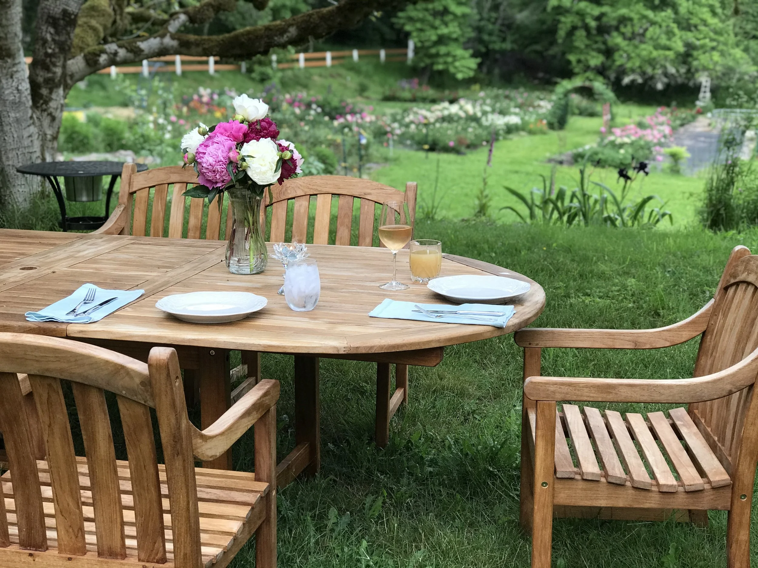 Long outdoor table set for a celebration with a white tablecloth, floral centerpieces, and place settings featuring gold utensils, beige plates, and white napkins. Celebrate a bridal shower, baby shower or bachelorette party with a continuous floral.