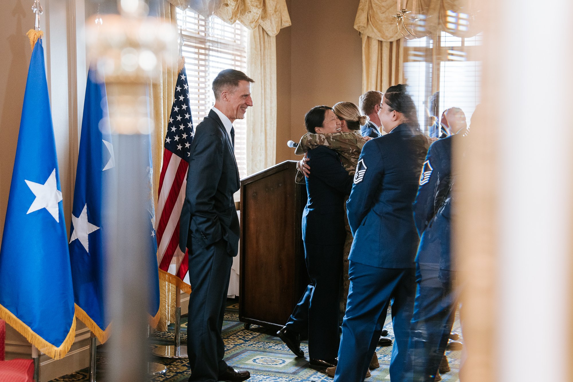 Military ceremony with people in uniform, American flags, and a podium in a decorated room.