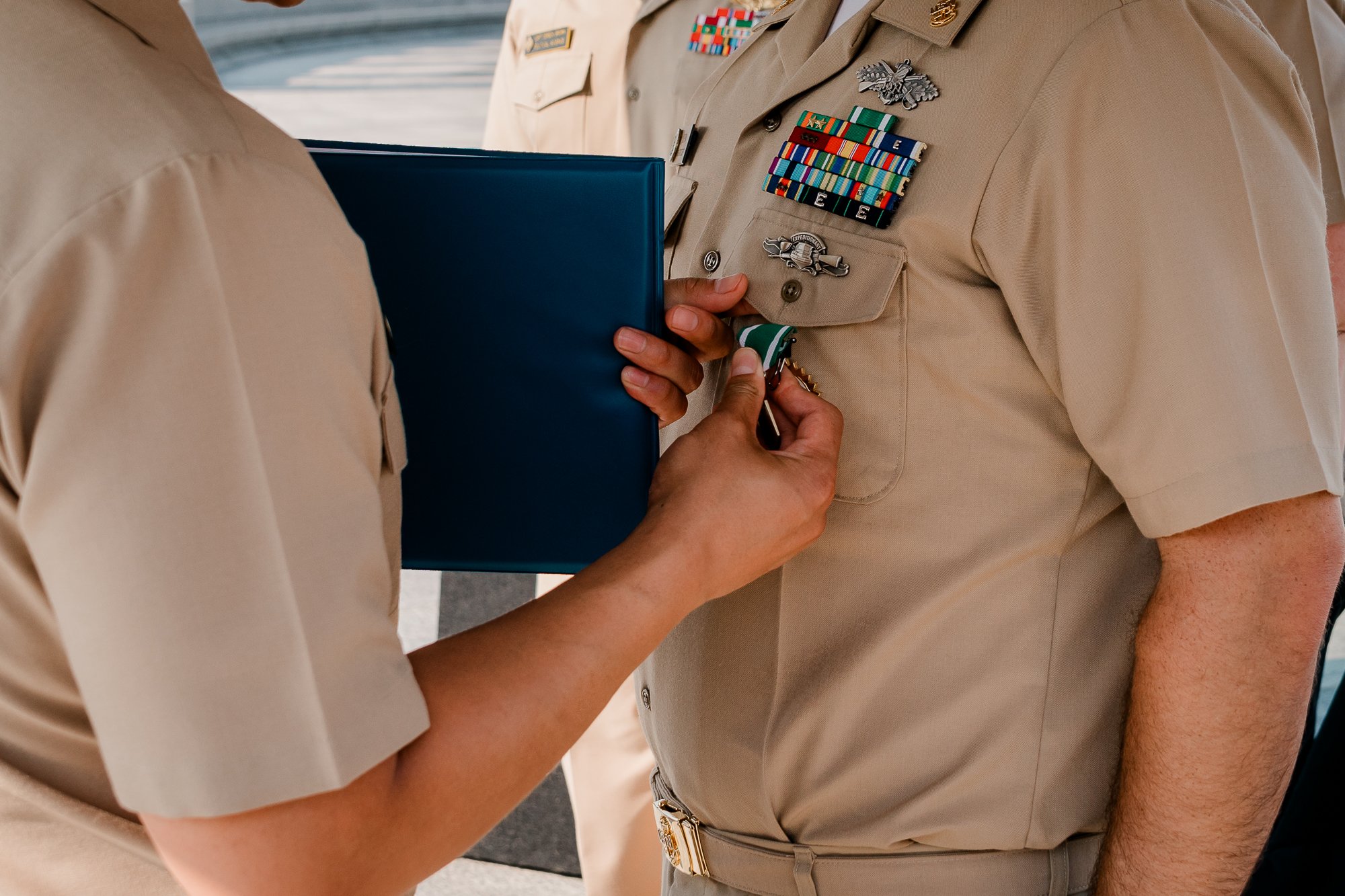 Military personnel in uniform, awarding a medal, with ribbons and badges displayed on the chest.