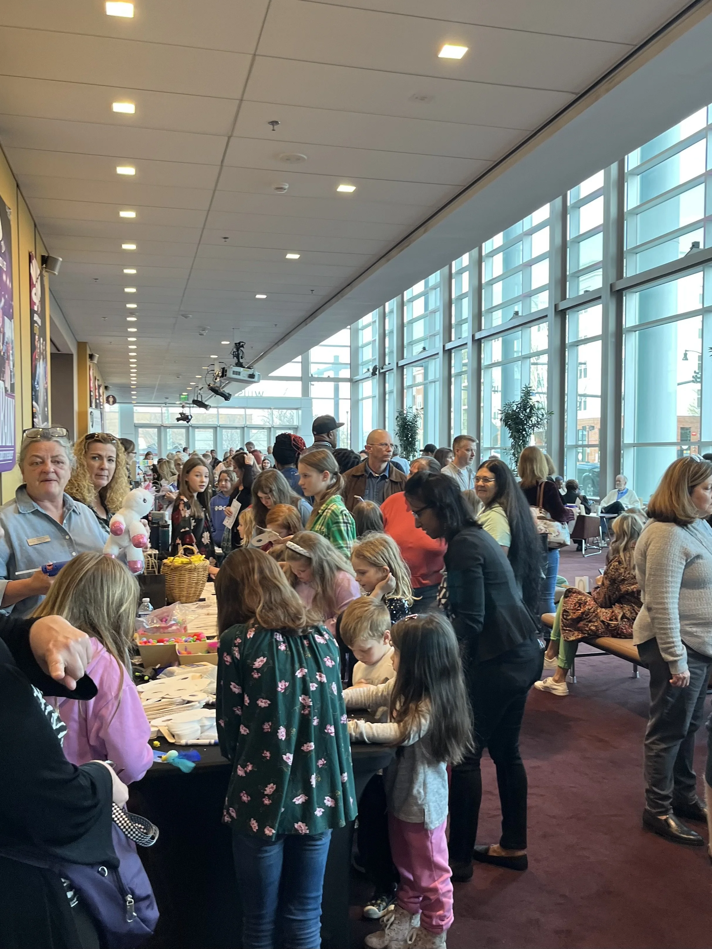 People gathered at an indoor event with children participating in a craft activity at a long table.