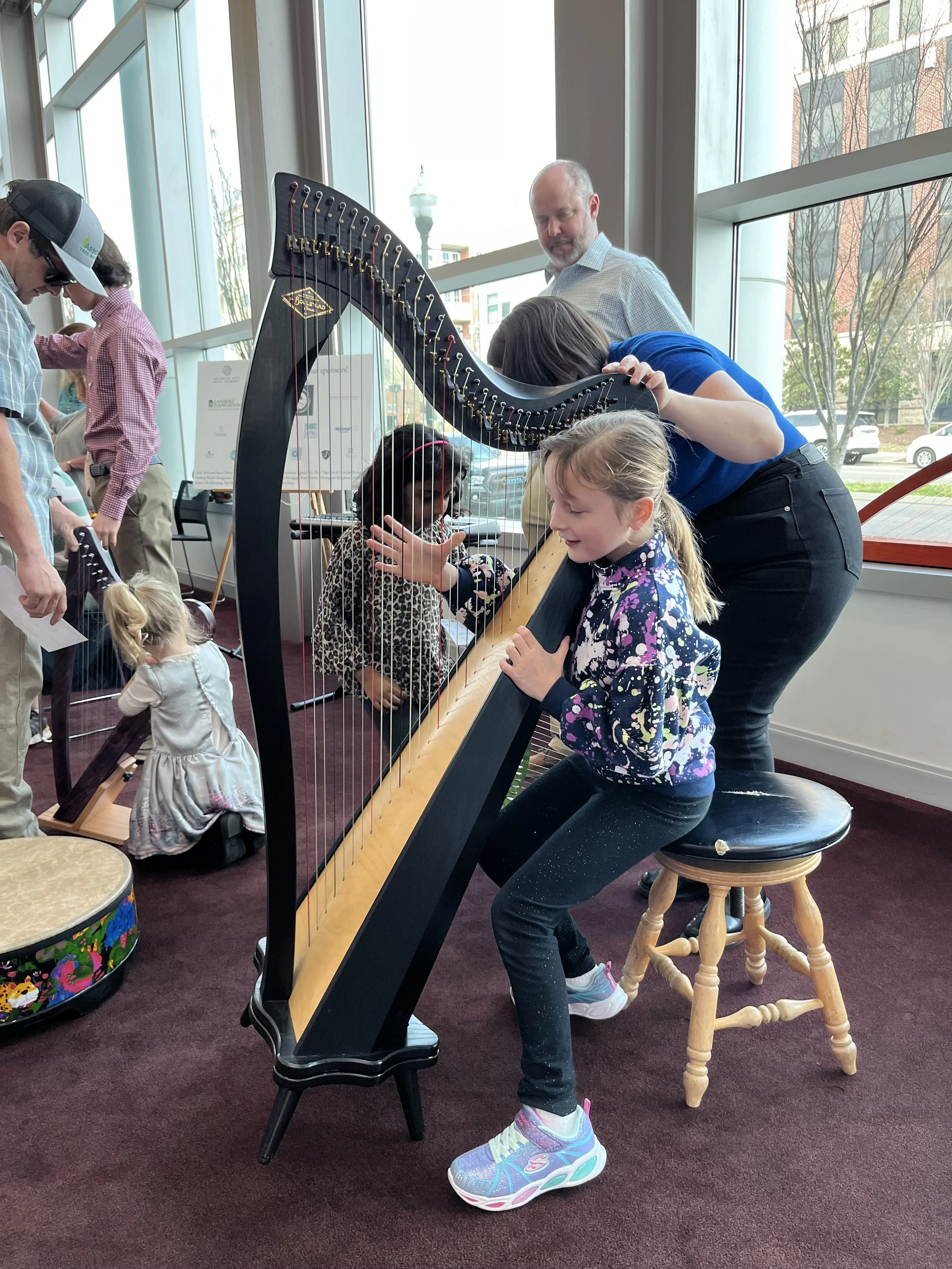 Children learning to play a harp with an adult's assistance.