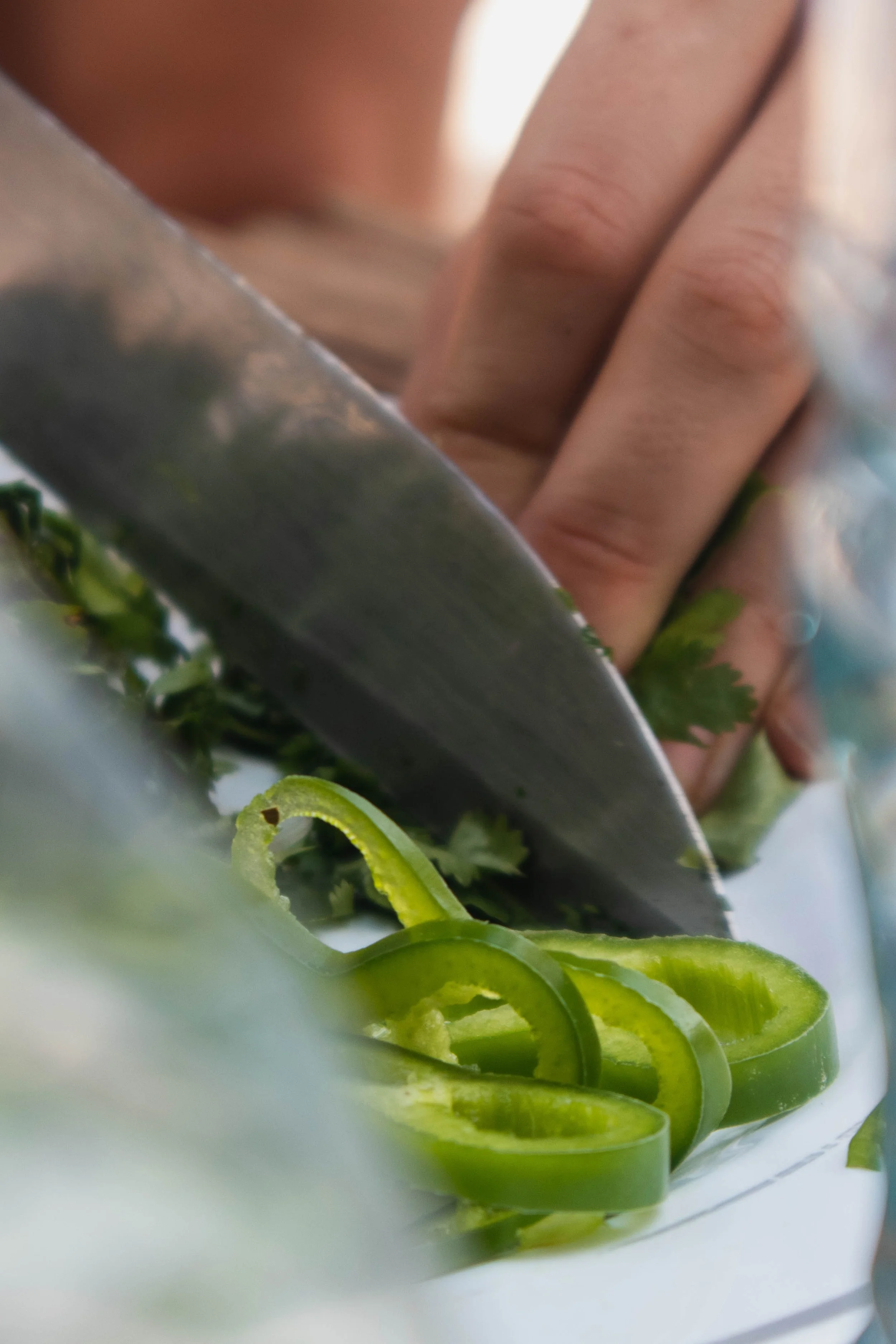 Close-up of a hand slicing green bell peppers with a knife on a cutting board.