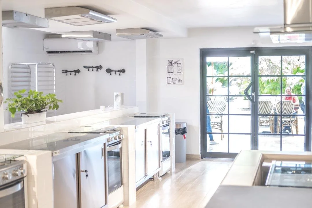 Modern kitchen with stainless steel appliances, potted plant, large windows showing outdoor seating area.