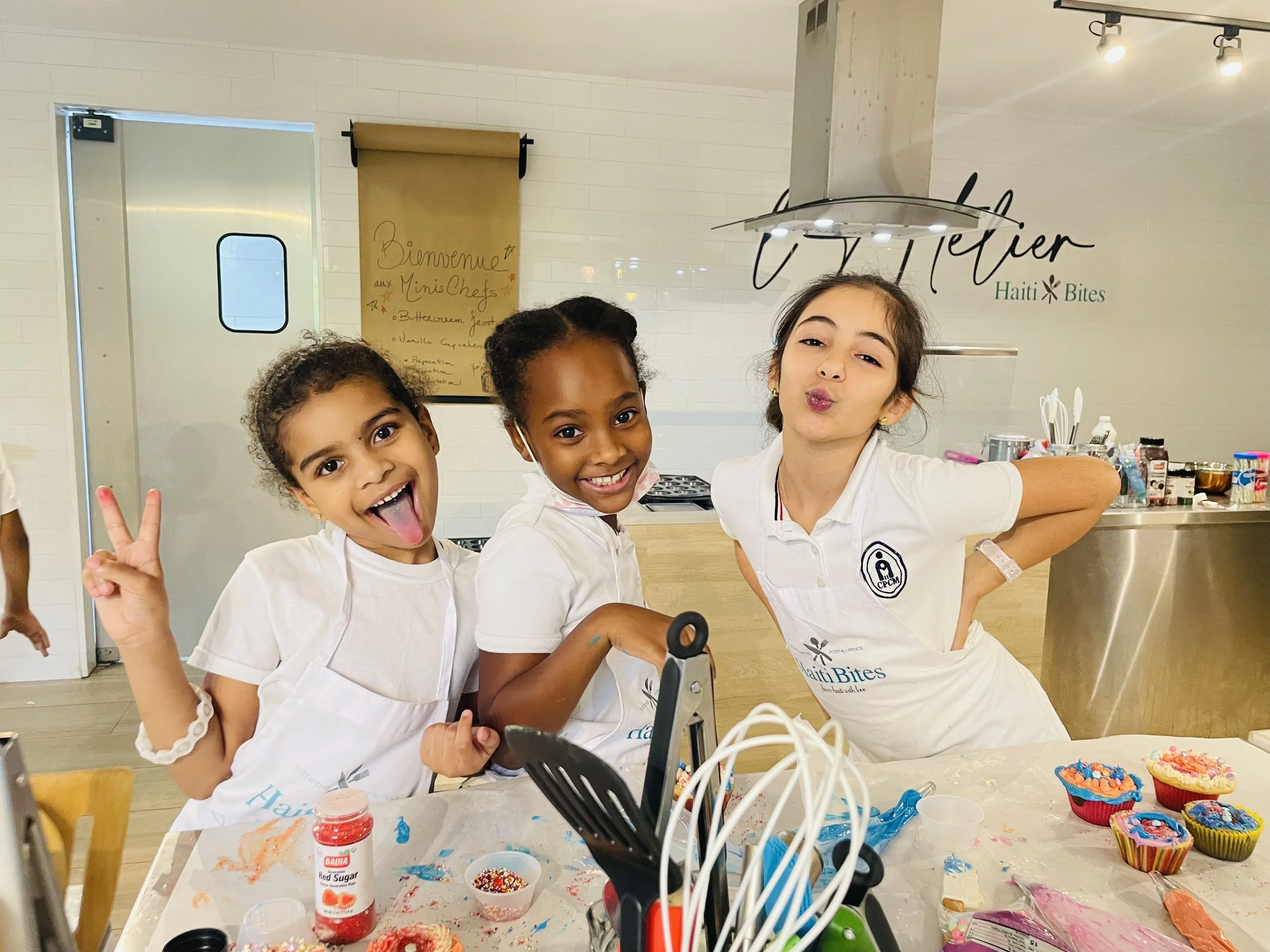 Three children in aprons having fun at a cooking class with cupcakes and frosting on the table.