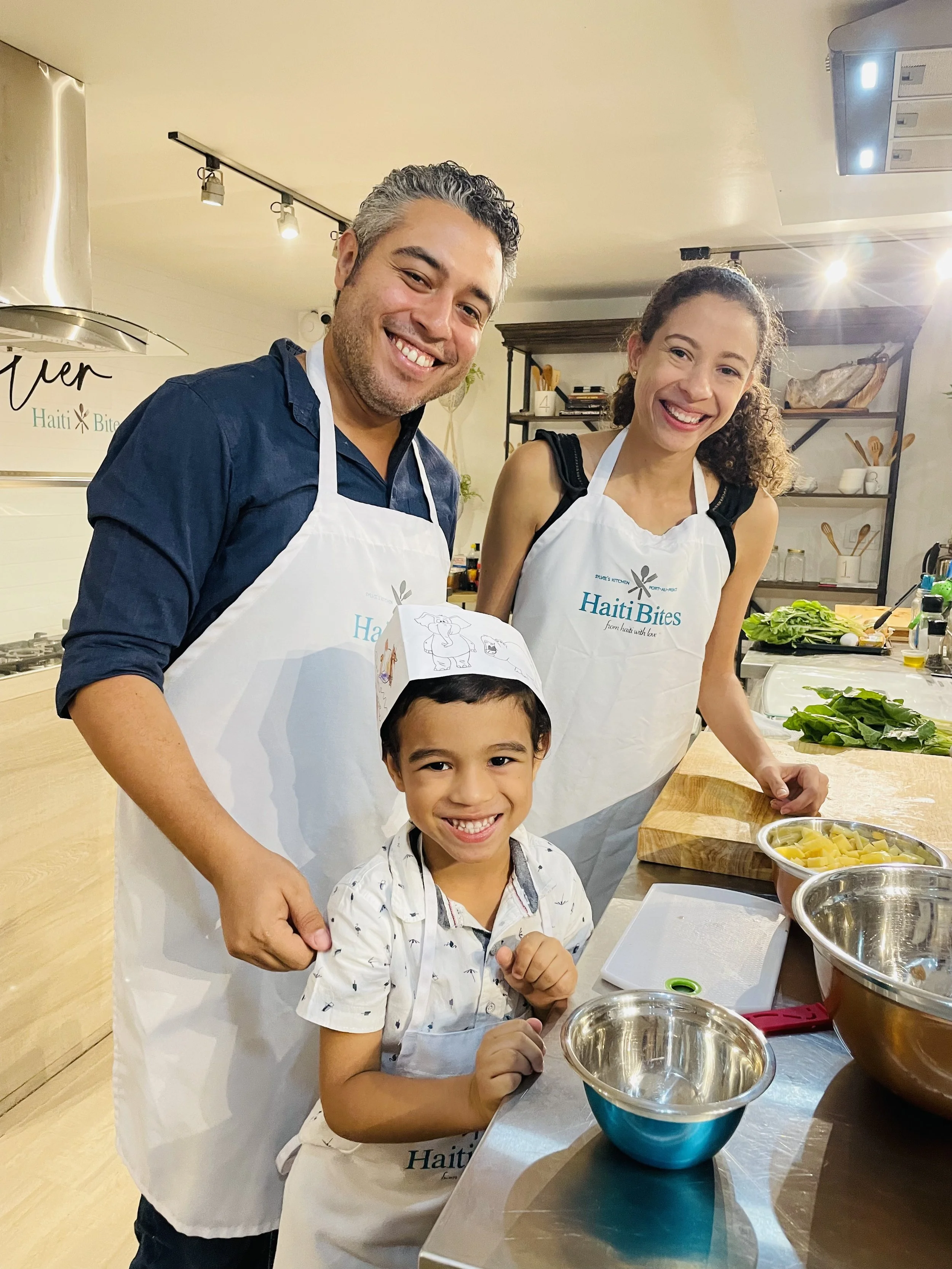 Family cooking together in a kitchen wearing aprons and smiling.
