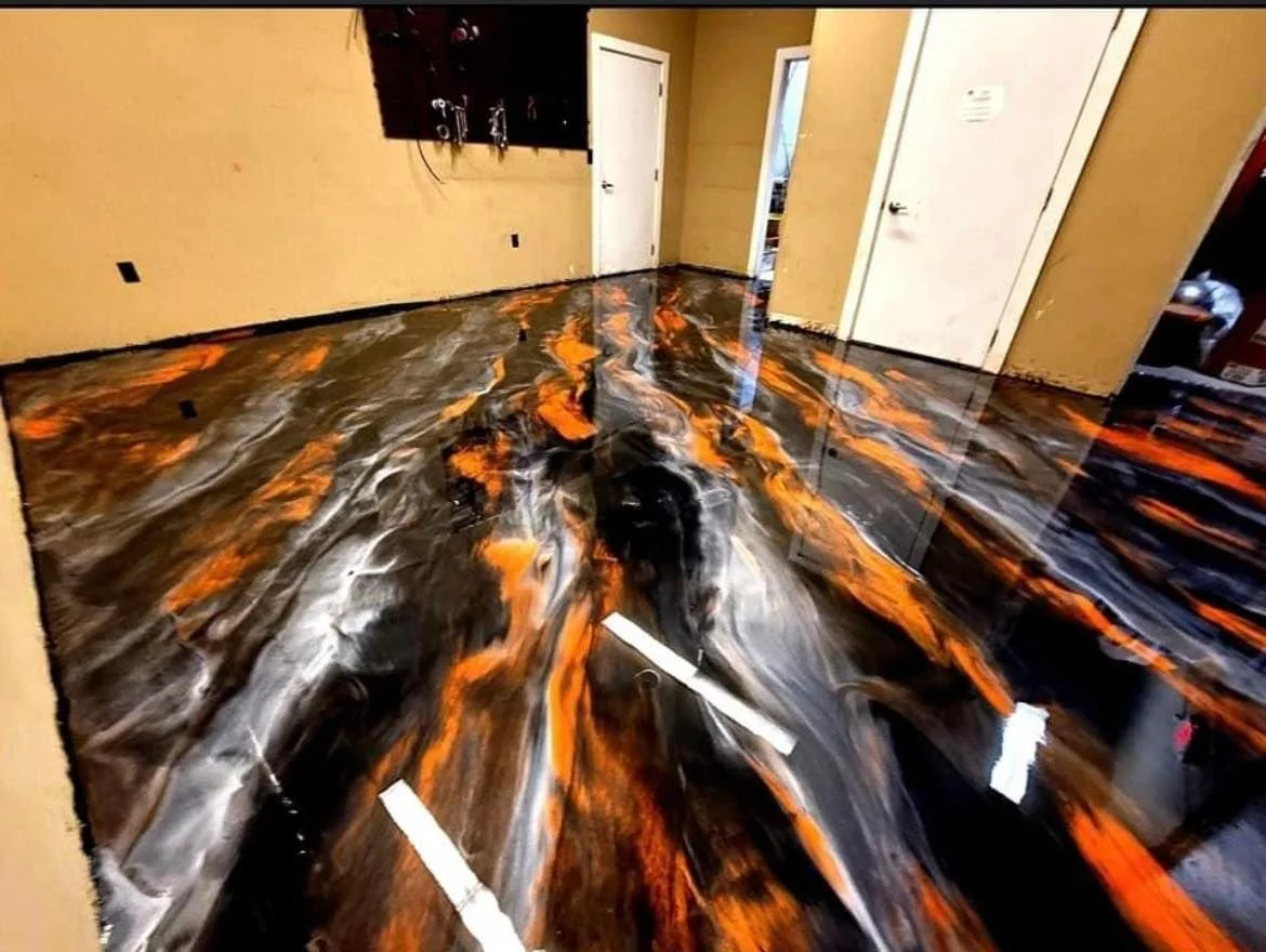 A room with a glossy, swirling black, orange, gray, and white metallic epoxy floor, beige walls, and a TV mounted on the wall.