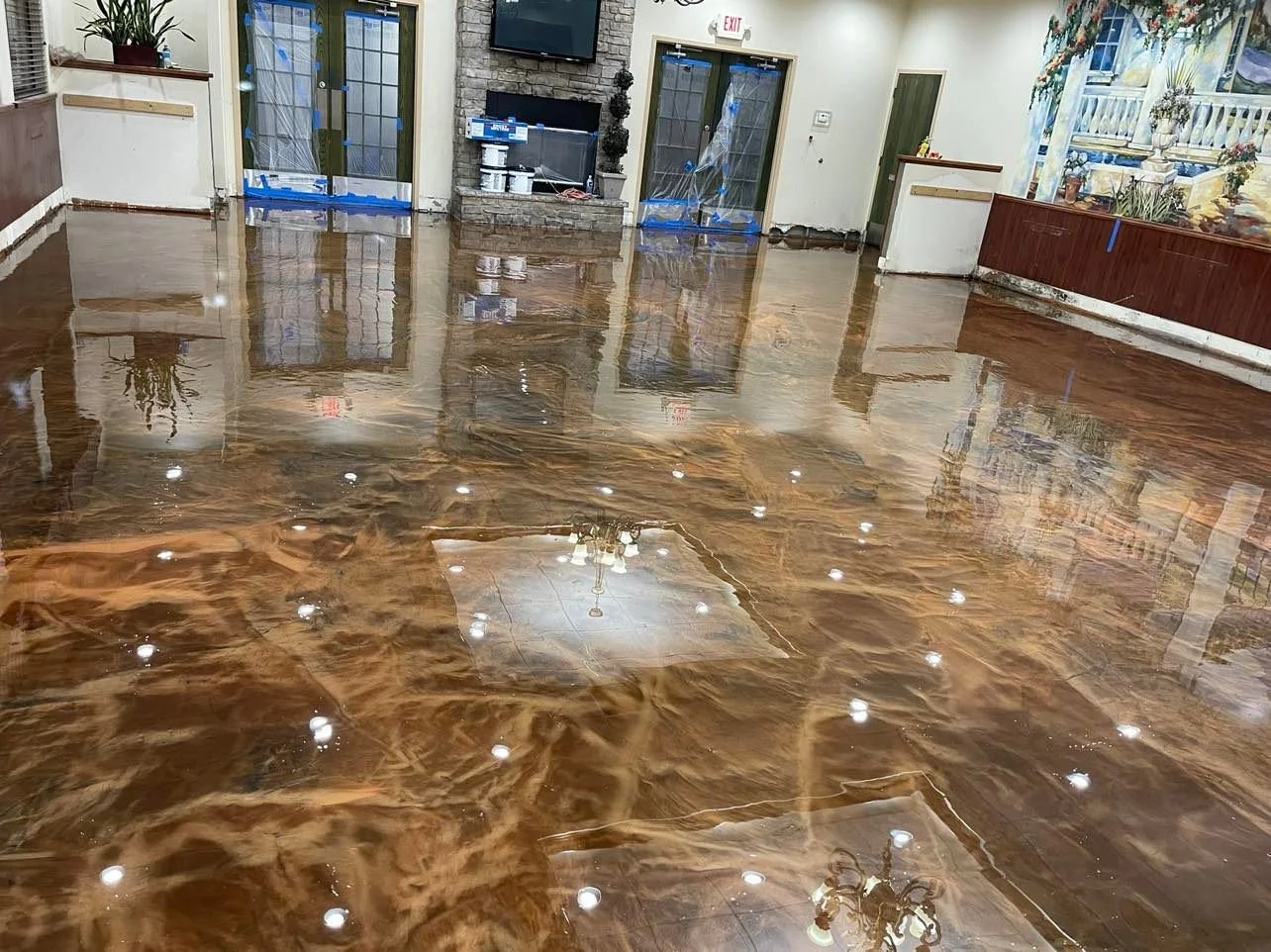 Interior room with new metallic epoxy floor, reflecting chandelier and ceiling lights, furniture, and a mural.
