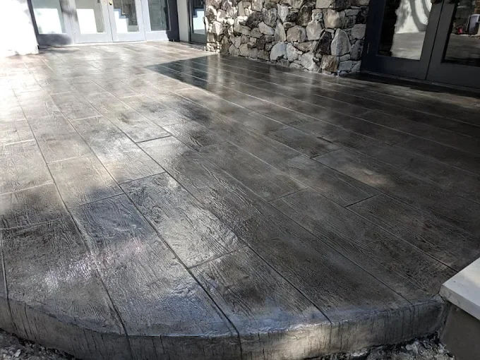 Close-up view of a polished concrete patio with large rectangular tiles and a rounded edge, adjacent to a stone wall and glass doors.