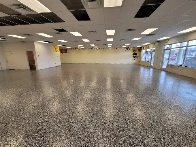 Empty commercial space with a speckled floor, white walls, and large windows