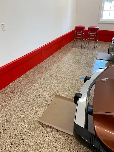 Empty room with red baseboard and two red barstools near a window, with a cardboard piece on the floor.
