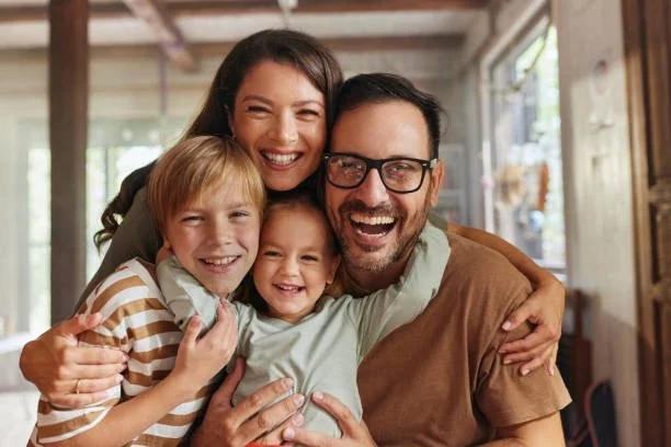 Happy family of four embracing indoors, smiling, with a woman, man, and two children