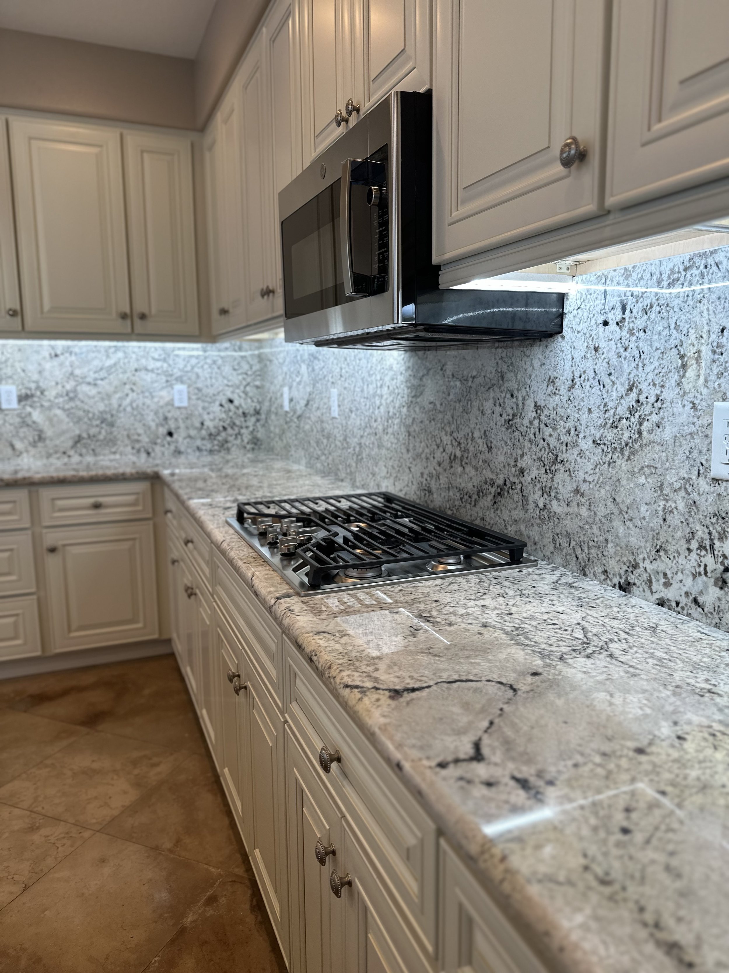 Kitchen countertop with granite surface, beige cabinets, stainless steel microwave, and built-in gas stove.