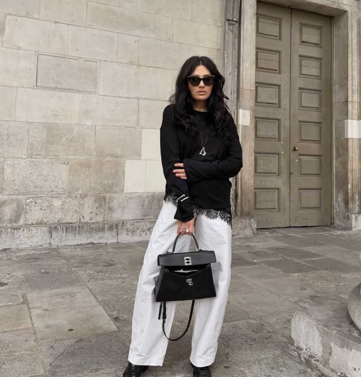 Fashion influencer wearing a black asymmetrical lace-trim camisole paired with white wide-leg trousers and a black designer handbag.