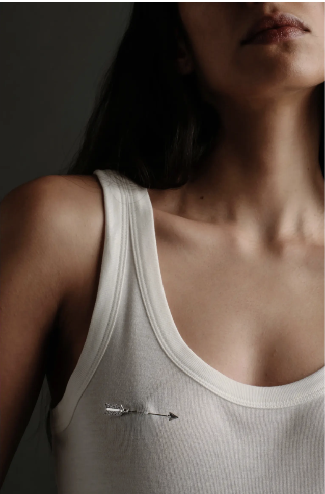 Awe Inspired gold Eros arrow brooch pinned to a white tank top