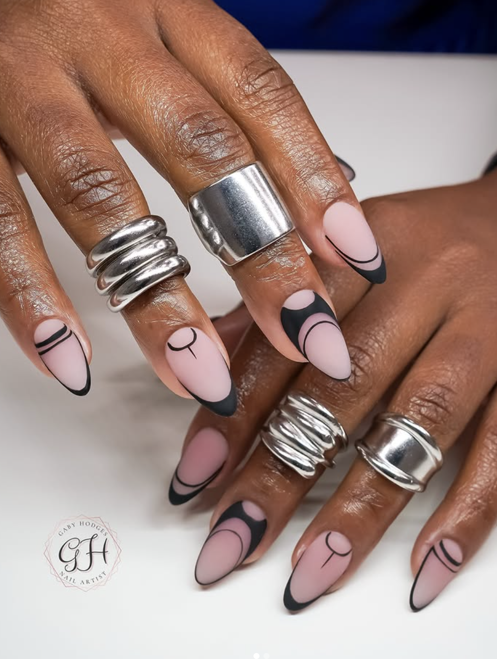 Almond-shaped nails featuring a modern matte pink base with black negative space French tips and fine geometric line accents.