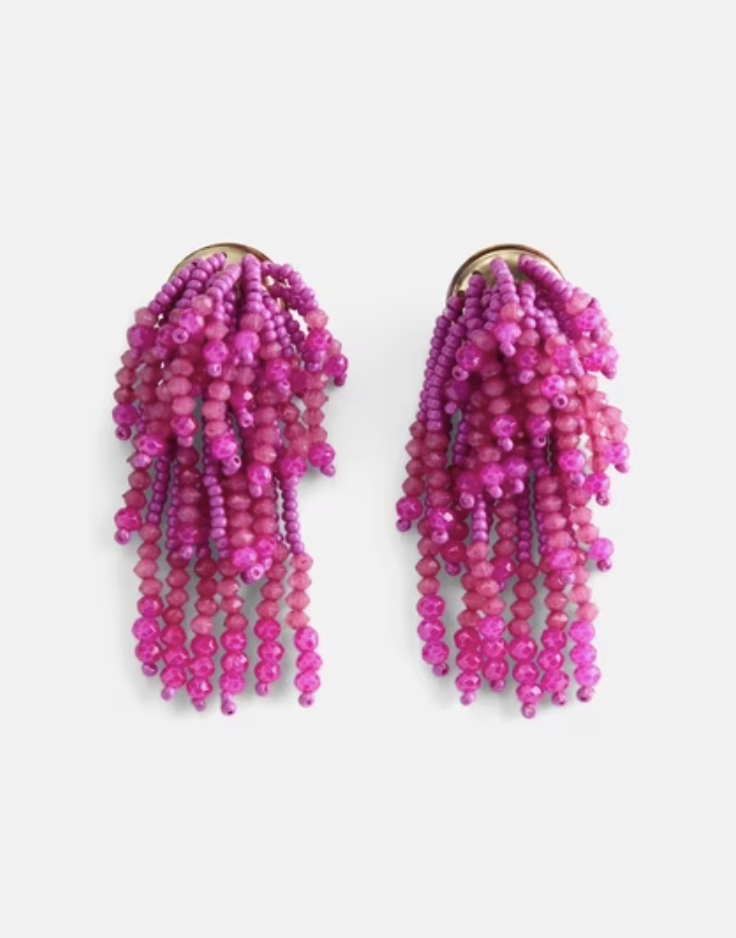 A close-up product shot of vibrant hot pink statement earrings featuring cascading beaded fringe strands hanging from a matching circular beaded post.