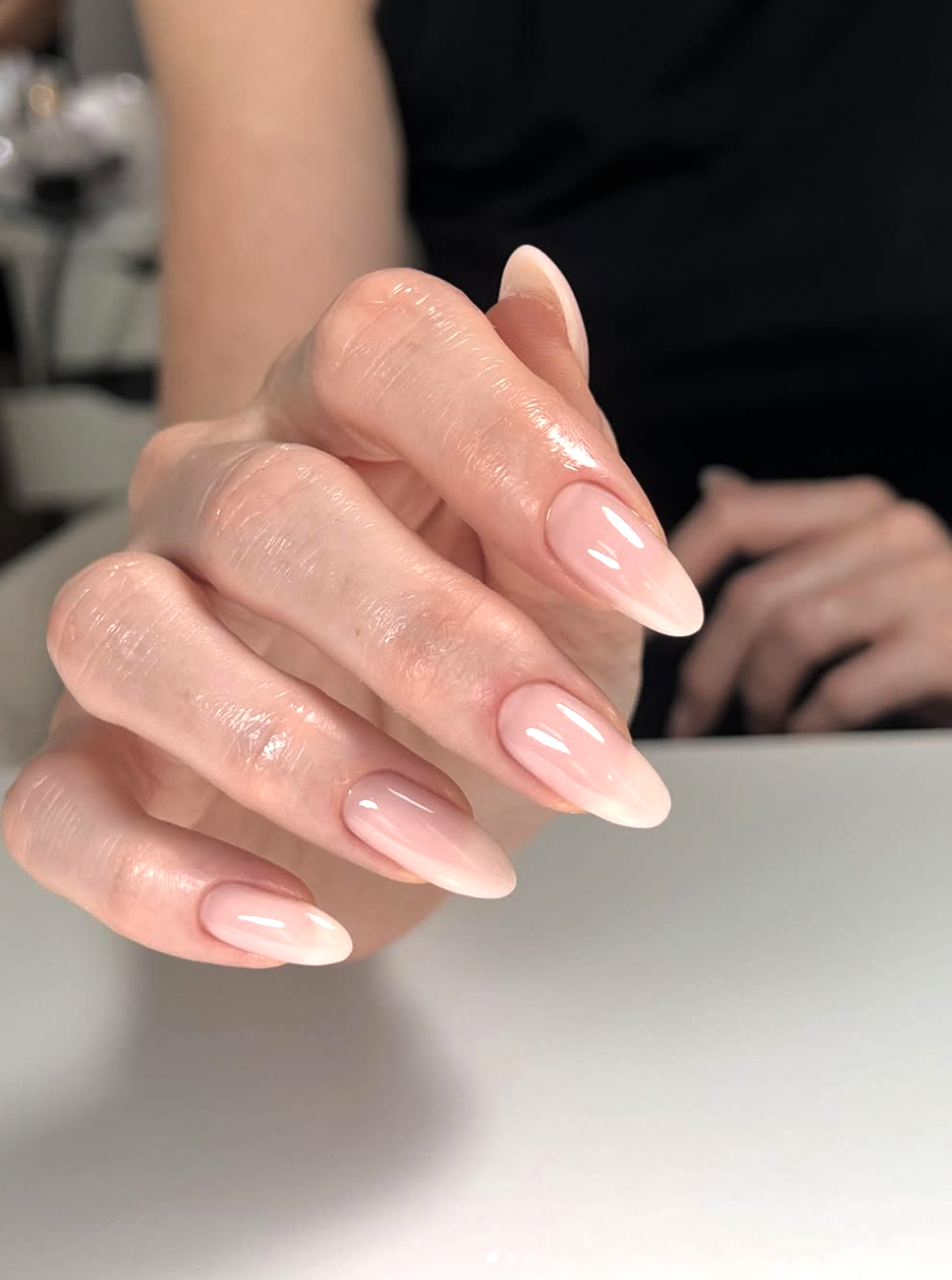Long tapered almond nails with a sheer peach-toned gloss and a clean, high-shine finish.