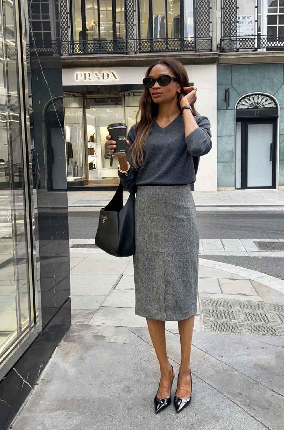 Woman wearing a gray tweed pencil midi skirt with a gray V-neck sweater and black patent pumps