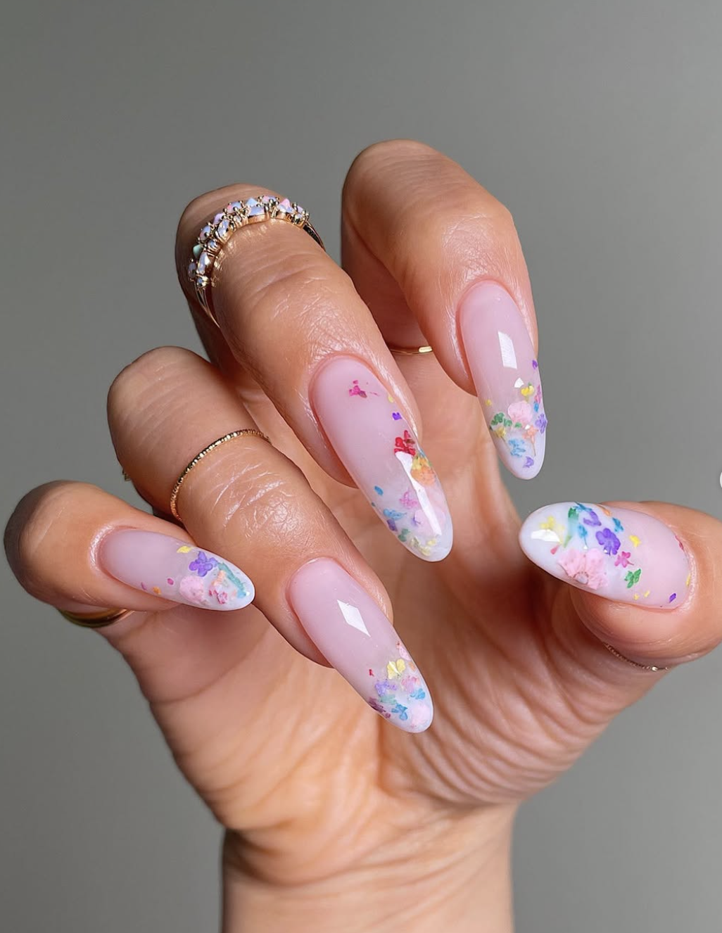 Long oval milky white nails with delicate, colorful hand-painted wildflowers and green leaves scattered across the base.