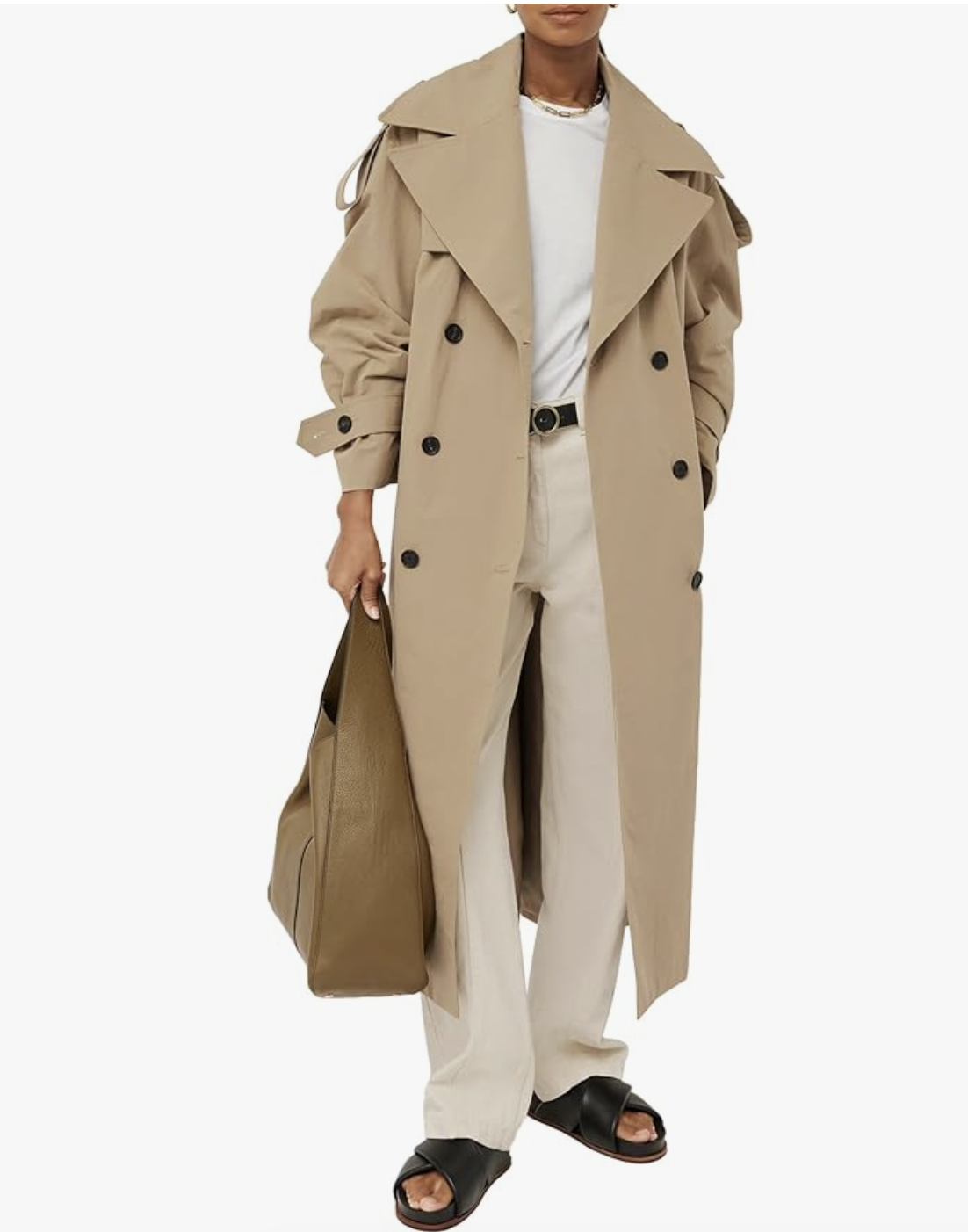 A woman wearing a tan, oversized double-breasted trench coat with a belted waist and structured lapels, styled with white trousers and black sandals for a clean spring look.