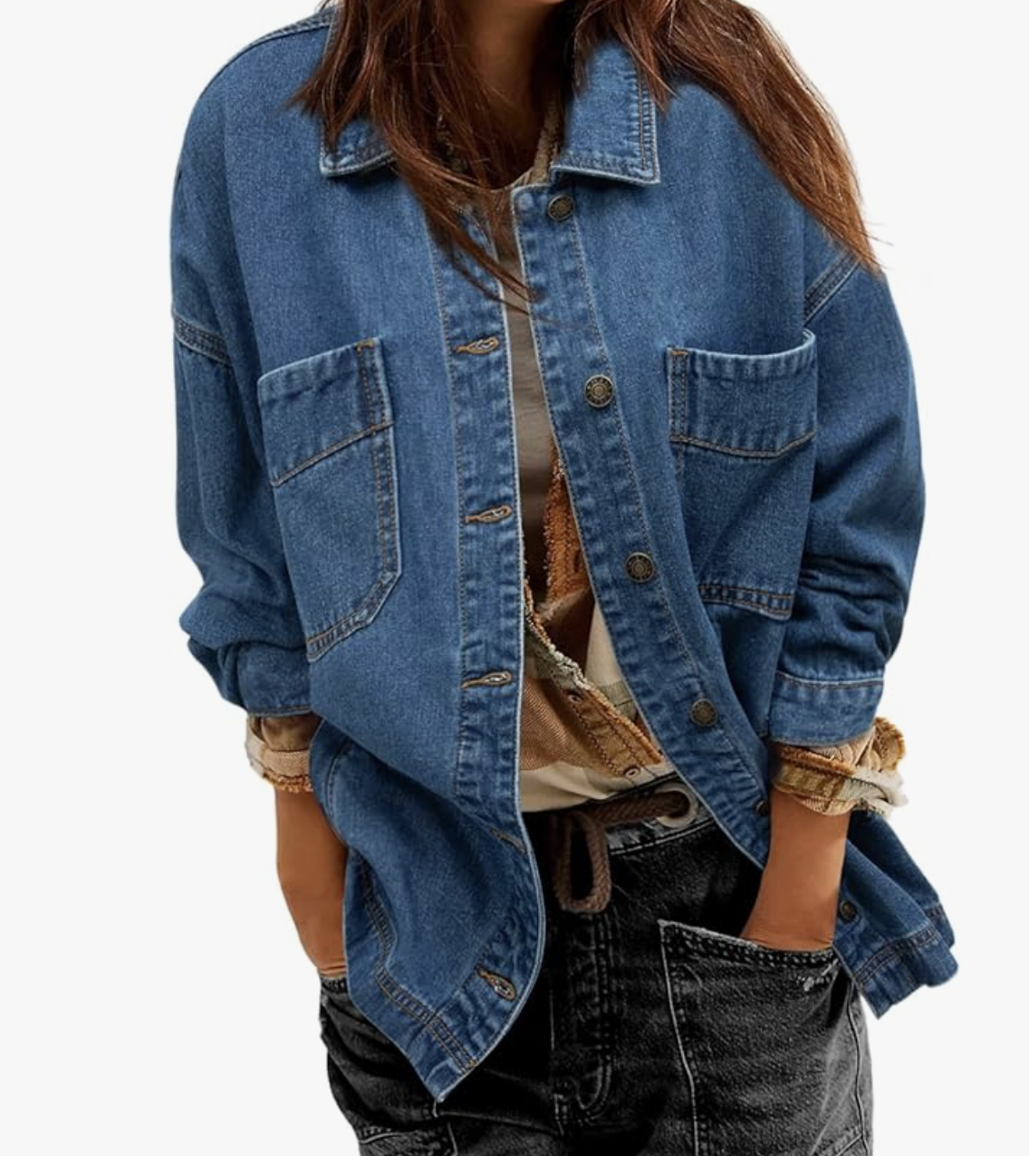 Front view of a woman wearing a relaxed, oversized mid-wash blue denim jacket with large front flap pockets and metallic buttons, layered over a tan textured shirt and black jeans.