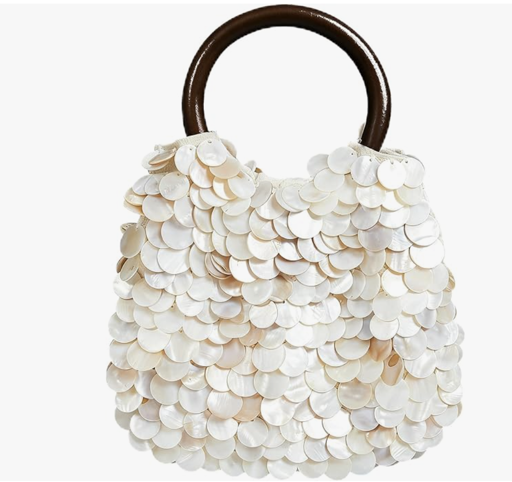 A white textured seashell-shaped clutch purse with a dark wooden handle, styled as a statement accessory for a Mediterranean beach vacation outfit.
