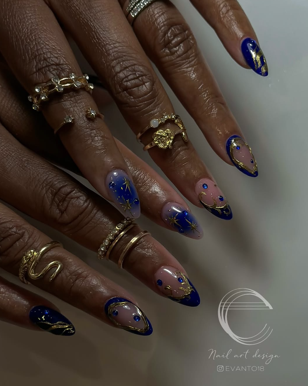 Long, oval-shaped nails featuring a deep navy blue base coat decorated with intricate hand-painted gold starbursts, celestial micro-dots, and crescent moons.